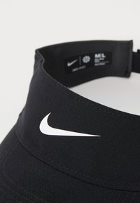 Svart Nike solhatt laget av lett stoff, med en hvit logo på fronten. Inkluderer en etikett med størrelse og vaskeinstruksjoner.