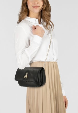 Schwarze Lederhandtasche mit einer Umschlagklappe, verziert mit einem metallischen, insektenförmigen Akzent und einem silbernen Kettenriemen. Glatte Textur und elegantes Design.