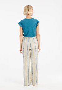 Turquoise short-sleeve top met ruches op de schouders, gecombineerd met gestreepte, wijde broek met verticale strepen in blauw, geel en beige.