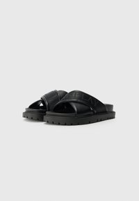 Chinelos pretos com design de tiras cruzadas, feitos de couro liso e tecido, apresentando uma marcação texturizada e uma sola espessa com aderência.