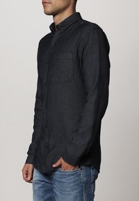 Camicia button-up in denim scuro. Presenta maniche lunghe, una tasca sul petto e bottoni marroni. Tessuto liscio con un motivo sottile.