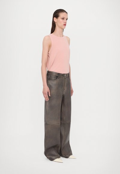 Top sin mangas de color rosa suave combinado con pantalones de pierna ancha marrón oscuro que presentan costuras visibles y una cremallera frontal. La modelo muestra una pose neutral.