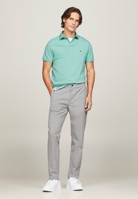 Camisa de polo verde menta con cuello, pantalones de cuadros grises y zapatillas blancas. La camisa presenta un pequeño logo en el pecho.