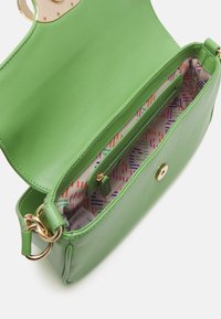 Bolso de mano de cuero verde con acabado brillante, que cuenta con un cierre dorado y un forro interior estampado en colores y formas vibrantes.