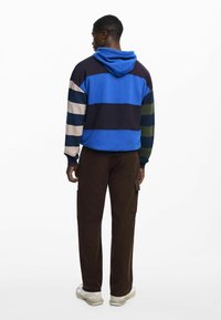 Hooded sweatshirt in blue, navy, and green horizontal stripes; paired with brown cargo pants. Features a relaxed fit and soft fabric.