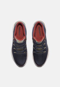 Para granatowych i czerwonych sneakersów Timberland z białymi podeszwami, widocznym logo na języku i wewnętrznej podeszwie, widziana z góry na białym tle.