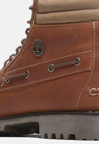 Gros plan d'une botte de randonnée en cuir marron avec col rembourré, œillets métalliques, détails cousus et semelle noire robuste à crampons.