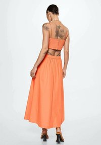 Orange to-delt outfit med en cropped top med justerbare stropper og et langt, svajende skørt med elastisk talje.