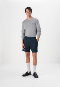 Gray long-sleeve sweater, navy textured shorts, white socks, and black loafers. Features a small green logo on the sweater.
