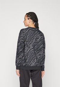 Felpa nera con motivo a strisce grigie a forma di tigre, scollatura a girocollo e polsini a costine, abbinata a pantaloni scuri, vista da dietro.