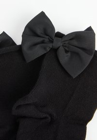 Sorte sokker med et tekstureret strikdesign og en stor satin sløjfe på hver manchet. Sløjferne er lavet af et glat, skinnende materiale.