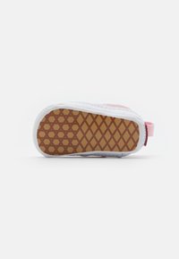 Suola di sneaker con un bordo bianco e parte inferiore in gomma marrone con un motivo a diamante. La parte superiore presenta un materiale rosa chiaro con una cinghia.
