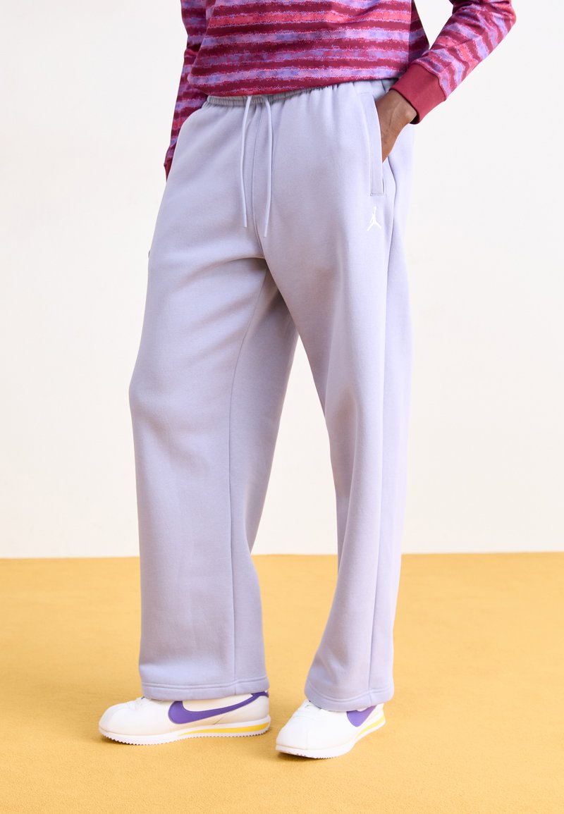 Lichtpaarse sweatpants met een elastische taille, zijzakken en een wit logo op de linkerdij. Gecombineerd met witte schoenen met paarse accenten.