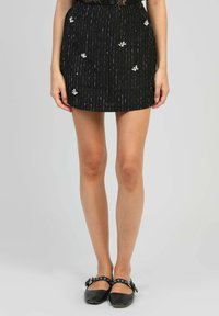 Jupe mini noire avec des rayures verticales et une broderie florale blanche. Le matériau semble texturé avec une taille ajustée. Associée à des ballerines noires.