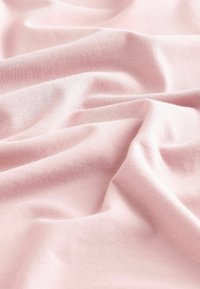 Ljust rosa bomullstyg med subtil textur och mjuka veck, som visar en slät och flexibel yta.