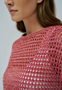 Strickkleid mit einem strukturierten, offenen Gewebemuster, das aus glänzendem rosa Garn besteht. Rundhalsausschnitt mit senkbaren Schulternähten, die die darunterliegende Haut freilegen.