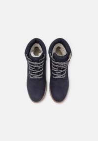 Botines de ante azul marino con un suave forro interior, cordones a rayas en gris y negro, y una suela marrón.