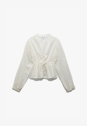 White, peplum blouse made of textured fabric. Features a deep V-neck, long sleeves, and a tie detail at the waist.