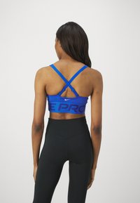 Modra športna modrček z X-hrbtnimi naramnicami in črnim napisom "NIKE PRO", v kombinaciji z visokimi črnimi legicami. Gladek material, prilegajoča se zasnova.