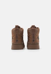 Brązowe wysokie trampki z teksturowanej tkaniny, z wyściełanym kołnierzem i pętelką do zakładania. Posiadają kontrastowe logo i solidną gumową podeszwę.