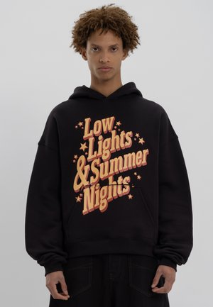 Schwarzer Kapuzenpullover mit einem großen, bedruckten Grafik in orange und gelbem Text, der "Low Lights & Summer Nights" liest, mit Sternenakzenten.