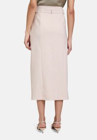 Helle rosa Midirock mit schmaler Taille, Gürtelschlaufen und Schlitze hinten. Glattes Material mit tailliertem Schnitt. Getragen mit beigen Absatzschuhen.