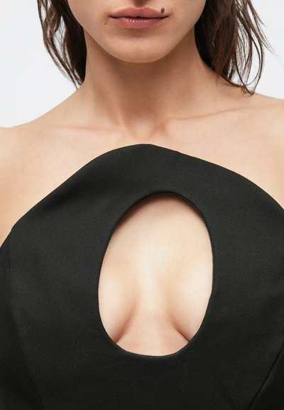 Μαύρο φόρεμα με μεγάλο κυκλικό άνοιγμα στη λαιμόκοψη, με υφασμάτινη υφή και δομημένο σχεδιασμό που τονίζει τη σιλουέτα.