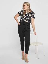 Floral-patterned navy blouse with short sleeves paired with black high-waisted trousers featuring a tie waist. Model wears neutral heeled mules.