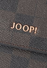 Superficie de cuero con un patrón a cuadros oscuro y letras metálicas doradas que forman la palabra "JOOP!" sobre un detalle de costura.