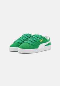 Gröna mockasneakers med vita accenter, rund tå, texturerad gummisula och gröna snören. Varumärkeslogotyp på tungan och sidan.