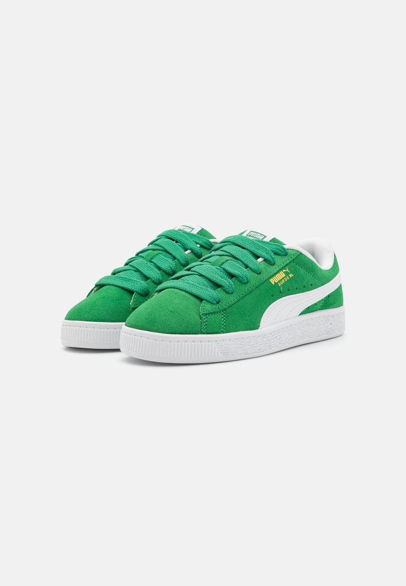 Baskets en daim vert avec des accents blancs, présentant un bout rond, une semelle en caoutchouc texturée et des lacets verts. Logo de la marque sur la languette et sur le côté.