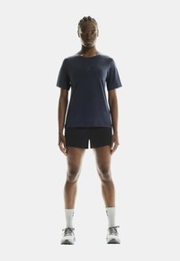 Sötétkék, rövid ujjú sportpóló fekete rövidnadrággal párosítva, fehér zoknikkal és szürke sportcipővel, amely kék részletekkel rendelkezik.