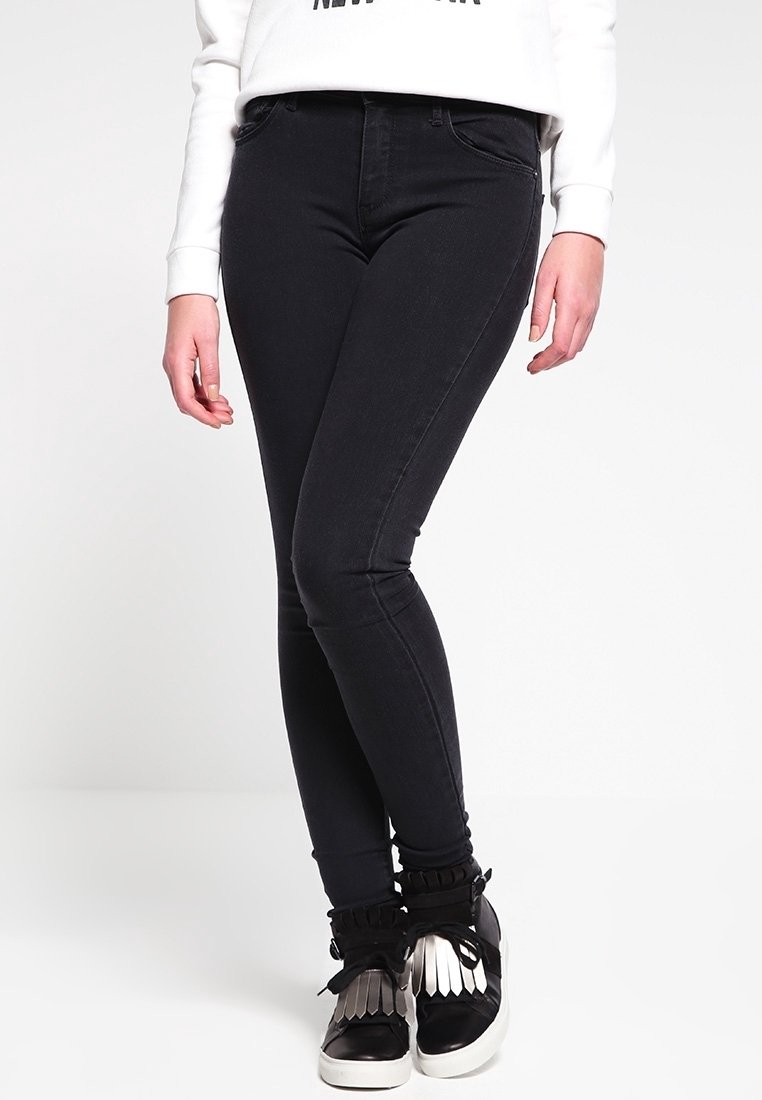 Jean skinny noir en denim avec une texture lisse, taille haute et design classique à cinq poches, associé à des baskets noir et argent.