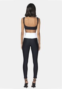 Top corto nero abbinato a leggings neri con una vita alta arricciata bianca. La modella indossa tacchi neri con cinturini e si trova su uno sfondo bianco.