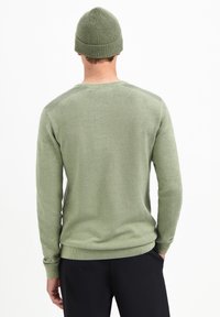 Groene gebreide trui met lange mouwen, gestructureerde stof, ronde halslijn en geribde manchetten. Gecombineerd met een bijpassende gebreide muts.