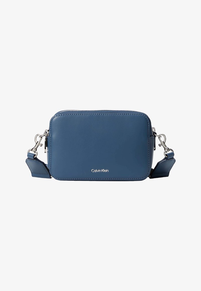 Petit sac bandoulière rectangulaire en cuir bleu avec fermeture éclair argentée, sangle amovible et logo Calvin Klein au centre à l'avant.
