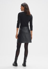 Mini gonna in pelle nera con un design a patchwork, abbinata a una maglietta attillata nera e collant neri opachi. Stivaletti neri chunky completano il look.