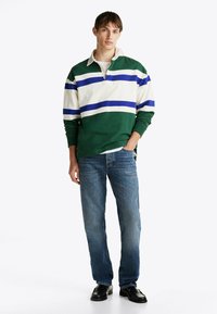 Grønne, hvide og blå stribede langærmede polo med krave, parret med lyseblå jeans og sorte sko.