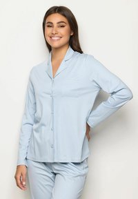 Pigiama a maniche lunghe azzurro chiaro con colletto, chiusura con bottoni e tasca, abbinato a pantaloni coordinati. Tessuto morbido al tatto.