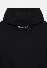 Sweatshirt à capuche noir en tissu doux, avec un col montant et le logo blanc "Calvin Klein" sur le col. Texture lisse, sans motifs.
