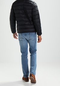 Giacca imbottita nera, jeans in denim blu, calzature marroni. Il materiale mostrato è liscio e testurizzato. La giacca presenta un design a righe orizzontali.