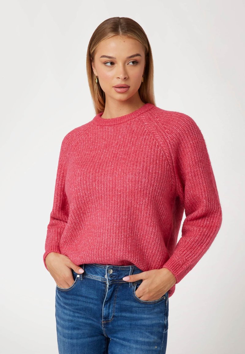 Maglione lavorato a maglia di un vivo rosa con texture a coste, scollo rotondo e maniche lunghe, abbinato a jeans in denim blu.