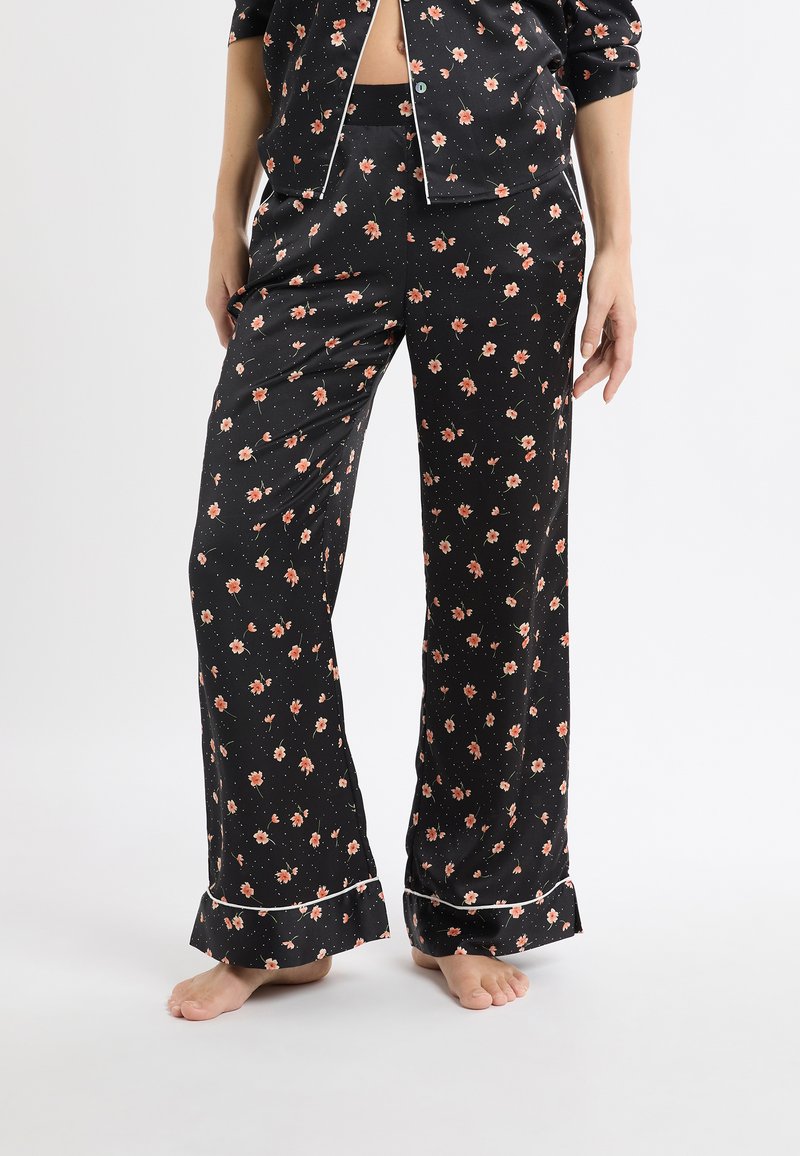 Czarny zestaw piżamowy z kwiatowym wzorem w różu i zieleni. Spodnie mają luźny krój i falbaniaste mankiety, uzupełnione białymi lamówkami.
