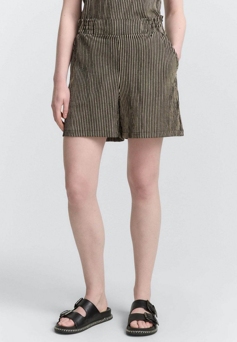 Svart och vit randiga shorts med avslappnad passform, med sidofickor och en mjuk tygtextur. Bärs med svarta sandaler.