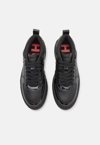 Schwarze Sneaker mit glänzender Lack-Oberfläche, ausgestattet mit schwarzen Schnürsenkeln, einem gepolsterten Schuhkragen und roten Logoakzenten auf den Innensohlen.