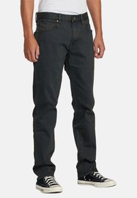 Jeans de mezclilla oscura con corte recto; cuentan con cinco bolsillos, cierre de botón y cremallera, y costuras sutiles. Llevados con zapatillas negras.