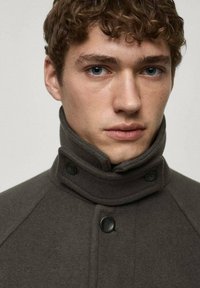 Dark grey wool coat with a high collar, featuring black buttons and a sleek, minimal design. Smooth texture, tailored fit.