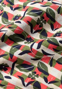 Bomullstyg med ett blommönster och bladen i marinblått, grönt, rött och krämfärgat, med en rutigt bakgrund och en mjuk textur.