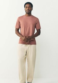 Camiseta de manga corta y cuello redondo en rosa apagado, combinada con pantalones beige claros, con un corte relajado y suave textura de algodón.