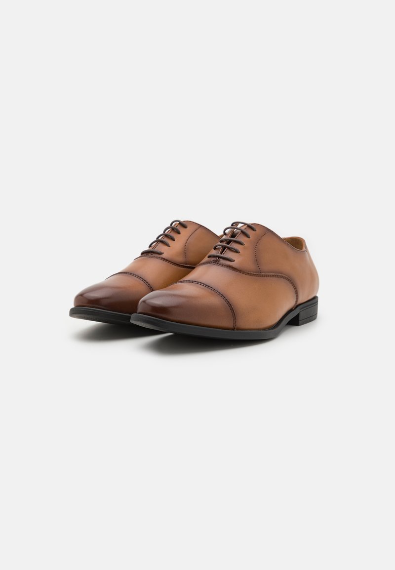Chaussures habillées en cuir marron avec une texture lisse, bout arrondi et lacets traditionnels. Présentent un petit talon en caoutchouc noir.